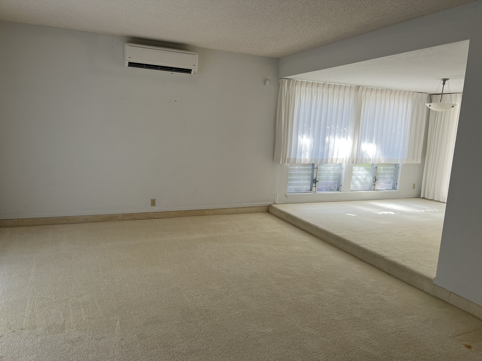 A room with a carpeted floor and a window with curtains.